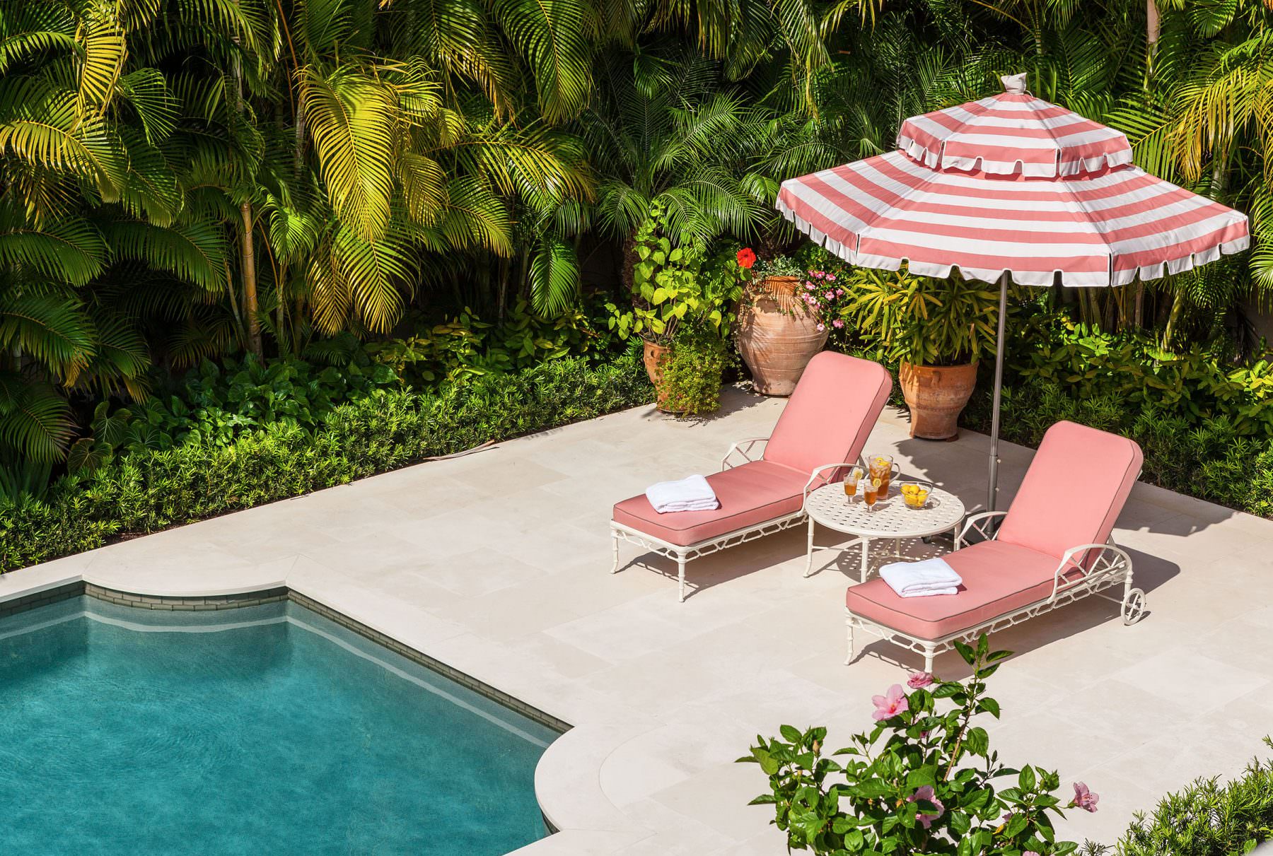Image of crystal blue pool with pink lounge chairs and striped pink and white umbrella.