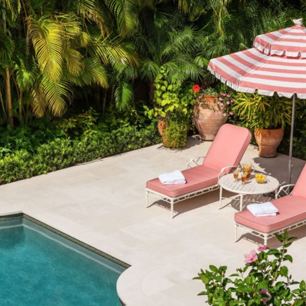 Pool with pink and white lounge chairs & umbrella with tropical floridan plants in the background.