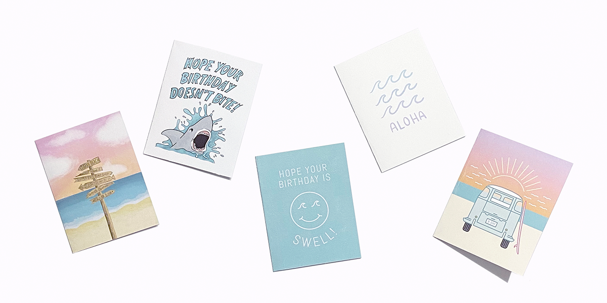 Greeting card designs created for Gypsy Life Surf Shop include a wooden way-finding sign with a beach sunset in the background, a shark illustration with hand lettering, a smiley face, waves with hand lettering, and a VW bus with sunset background.