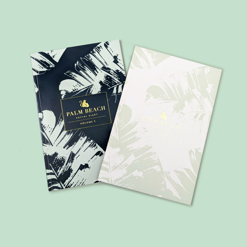 Volume 1 & 2 books for Palm Beach Social Diary, against a light green background. The books feature a light green tropical palm leaf pattern, on navy and white backgrounds, with the logo gold foiled on top.