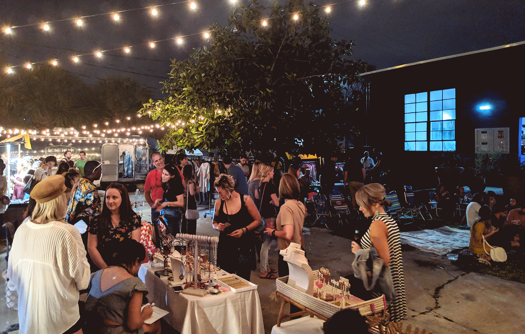 Crowd of party-goers are relaxing under the lights and night sky at Elizabeth Ave Station's pop-up event in West Palm Beach, FL.