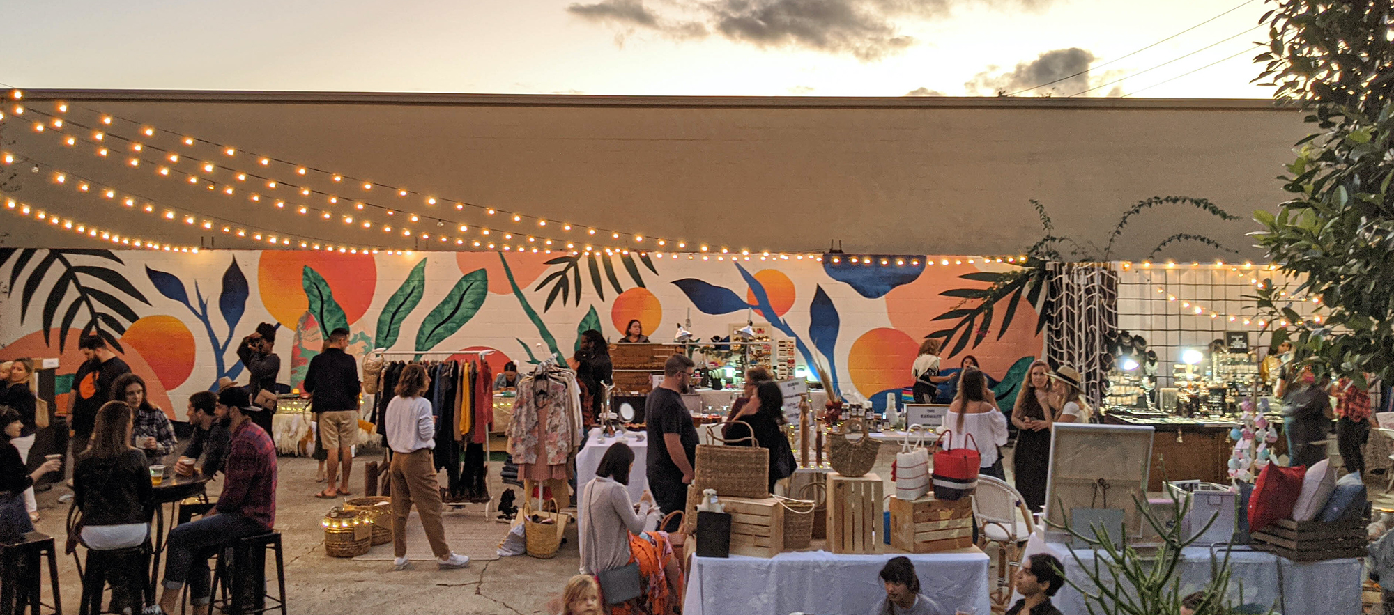 Crowd of party-goers in front of a bright and colorful botanical mural done by Melissa Deckert at Elizabeth Ave Station's pop-up event in West Palm Beach, FL.
