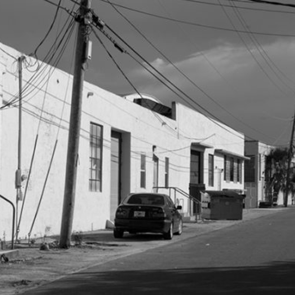 Black & white photo of West Palm Beach's Warehouse District on Elizabeth Ave with a row of old warehouses, telephone pole with wires & a car.