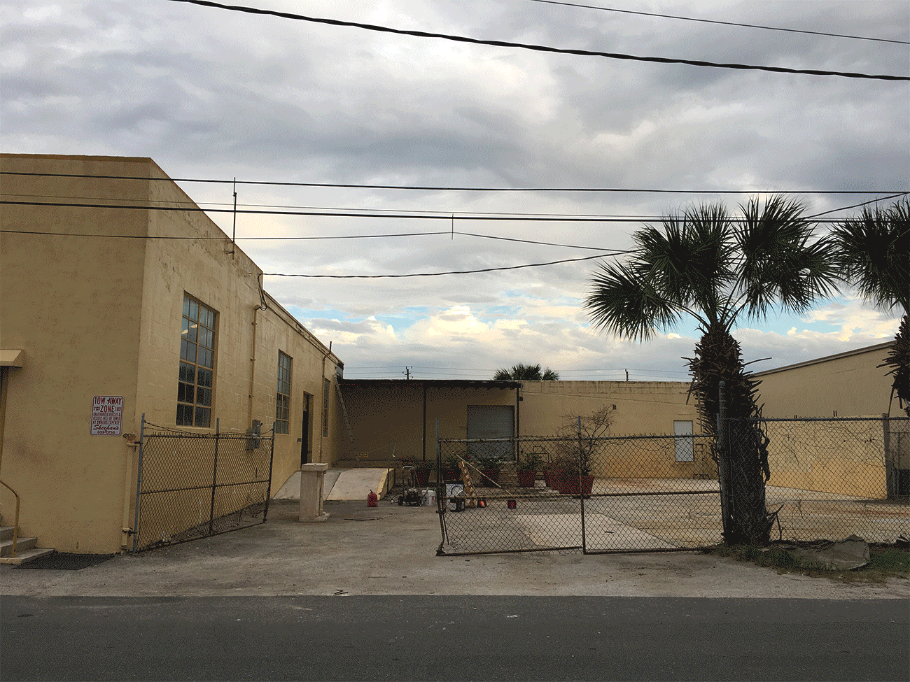 Run down looking yellow warehouse with a chain link fence and empty courtyard in West Palm Beach Florida