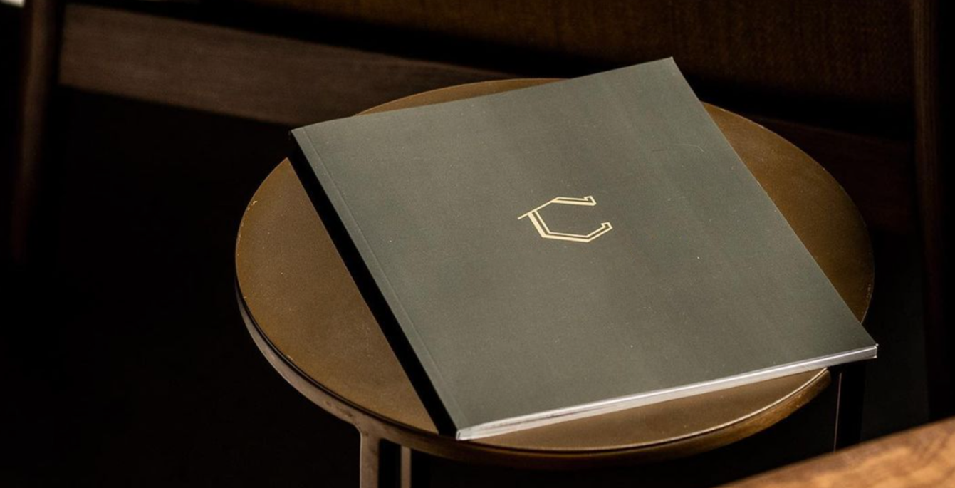 Compostion Coffee's icon mark featured on a deep brown journal placed on a wooden table.