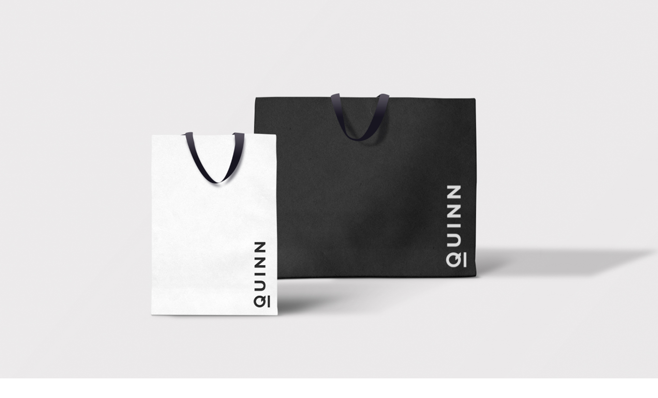Black and white shopping bag mockups with a vertical logo in the lower right hand corner of the bags in the inverted color, on a gray background.